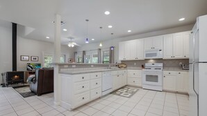 A modern kitchen with white cabinets, a built-in oven, and a dishwasher. There is a fireplace and a sofa in the adjacent living area. - Guadalupe River Rock Retreat 9740 by RedAwning (New Braunfels)
