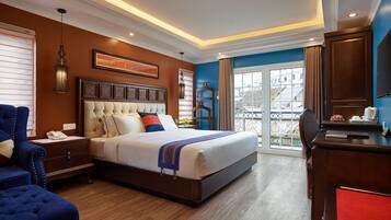 A hotel room with a large bed, a desk with a computer, a chair, and a view of the city through the window.