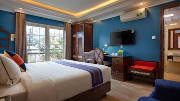 A hotel room with a large bed, a desk, a chair, a television, and a window with a view of buildings.