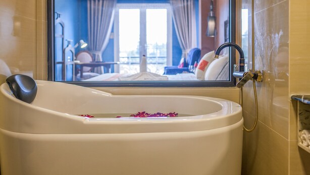 A bathtub with rose petals, a handheld showerhead, and a view of a bedroom through a glass door. - Eden Boutique Hotel & Spa (Sa Pa)