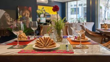A dining table set with plates, glasses, and a vase with a red flower.