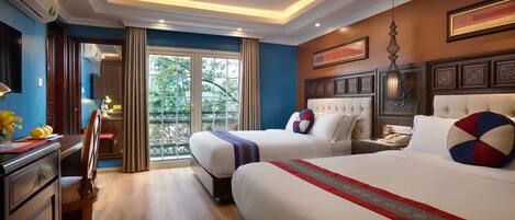 A hotel room with two beds, a desk, a chair, a desk lamp, a telephone, and a view of greenery through the window.