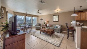 A spacious living room with a large window, a ceiling fan, a fireplace, and a dining area with a table and chairs.