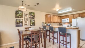 A kitchen with wooden cabinets, a dining table with chairs, a bar area, and a microwave. - Guadalupe Getaway Ww B201 2 Bedroom Condo by RedAwning (New Braunfels)