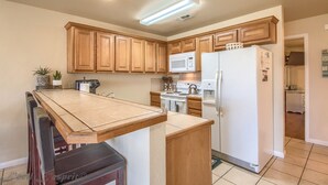 A kitchen with wooden cabinets, a microwave, a refrigerator, and a dining table with chairs. - Guadalupe Getaway Ww B201 2 Bedroom Condo by RedAwning (New Braunfels)