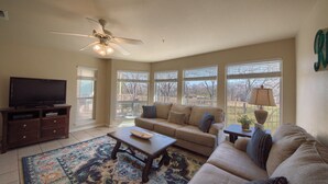 A living room with a ceiling fan, a television, a sofa, a coffee table, and large windows. - Guadalupe Getaway Ww B201 2 Bedroom Condo by RedAwning (New Braunfels)