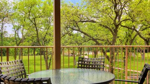 A covered outdoor area with a round glass table and four wicker chairs, surrounded by a metal railing and lush greenery. - Guadalupe Getaway Ww B201 2 Bedroom Condo by RedAwning (New Braunfels)
