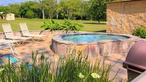 An outdoor hot tub area with lounge chairs and a stone wall.