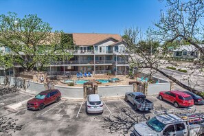 A multi-story hotel with a swimming pool, parking lot, and a view of the surrounding area.