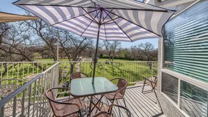 Un espace extérieur abrité, avec une table et des chaises, un parasol à rayures et une vue sur un paysage verdoyant.