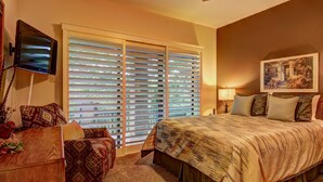 A bedroom with a large bed, a TV mounted on the wall, and a window with blinds. - River Remedy CWC110 by RedAwning (New Braunfels)