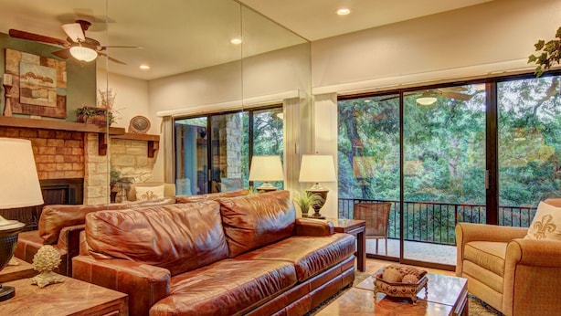 A spacious living room with a leather sofa, a fireplace, and large windows offering a view of trees. - River Remedy CWC110 by RedAwning (New Braunfels)