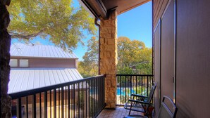 A balcony with a stone pillar, a metal railing, and a view of a swimming pool.