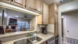 A kitchen with granite countertops, stainless steel sinks, wooden cabinets, a ceiling fan, and a coffee maker.