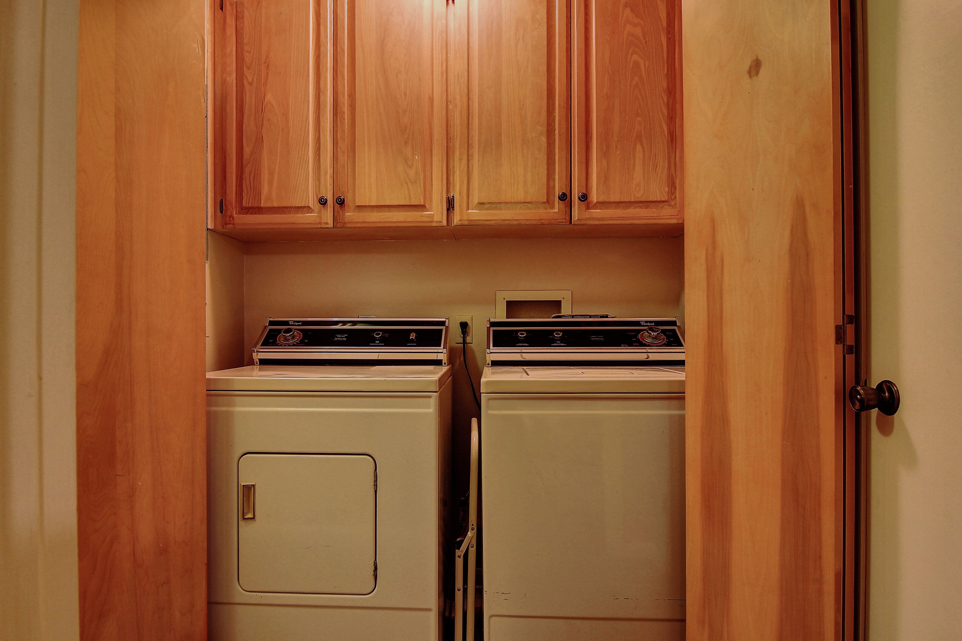 A laundry room with two stacked washers and dryers, wooden cabinets above, and a door on the right.