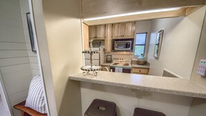 A compact kitchen with wooden cabinets, a microwave, an oven, and a small bar stool area.