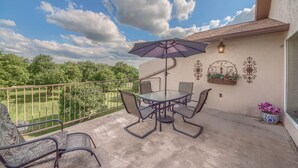 A balcony with a glass table and chairs, a purple umbrella, and a view of a green landscape. - River Vista Ww G302 2 Bedroom Condo by RedAwning (New Braunfels)
