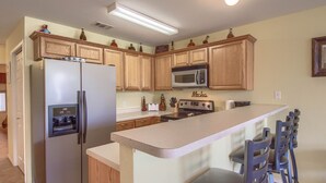 A kitchen with wooden cabinets, a refrigerator, a microwave, a stove, and a bar area with chairs. - River Vista Ww G302 2 Bedroom Condo by RedAwning (New Braunfels)