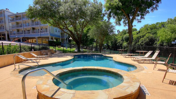 A swimming pool with a hot tub, surrounded by lounge chairs and a fenced area. - Grandma's River Haus       Rrc A108 1 Bedroom Condo by RedAwning (New Braunfels)