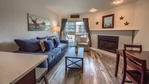 A living room with a sofa, coffee table, fireplace, and a painting of a bull. - Grandma's River Haus       Rrc A108 1 Bedroom Condo by RedAwning (New Braunfels)