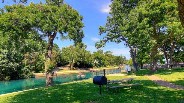 Un parc équipé d’une table de pique-nique, d’un barbecue et situé près d’une rivière.