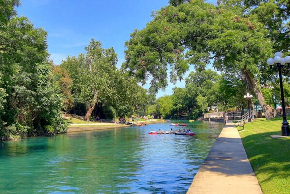 A river with boats, a walkway, and trees.