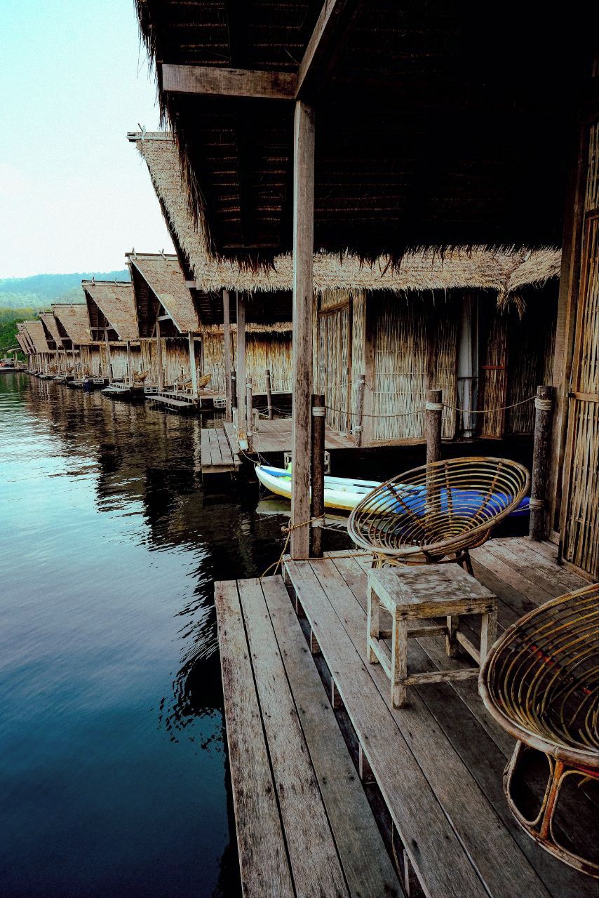 A row of wooden overwater bungalows with thatched roofs, connected by wooden walkways over calm water.