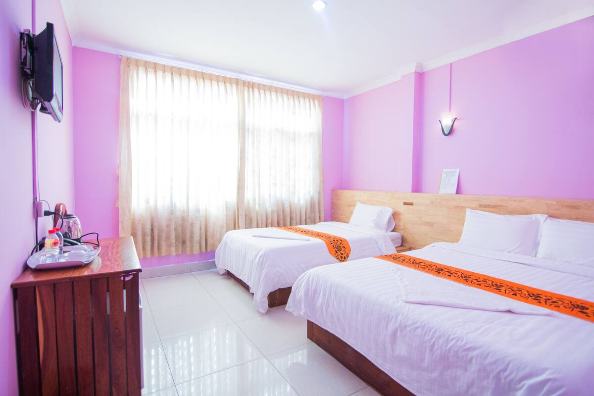 A hotel room with two beds, a wooden headboard, a desk with a computer and phone, and a window with curtains.