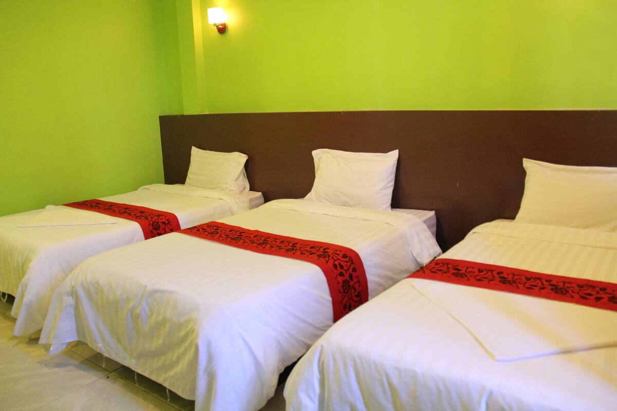 A hotel room with three single beds, each with white bedding and a red decorative border.