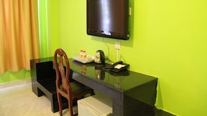 A room with a green wall, a flat-screen TV mounted on the wall, a wooden chair, a small table with a tray of drinks, a kettle, and a phone. - Kim Guesthouse (Phnom Penh)