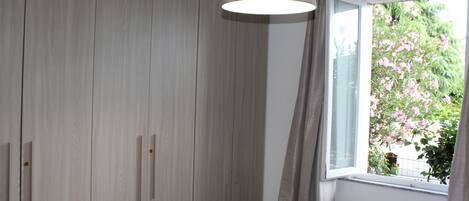 A room with a wooden wardrobe, a window with curtains, and a hanging light fixture.