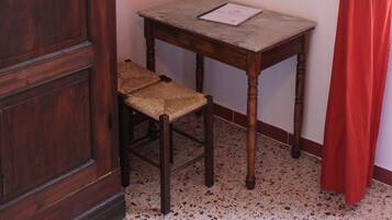 Una habitación con un armario de madera, una mesita con una silla, un cuadro en la pared y una cortina roja.