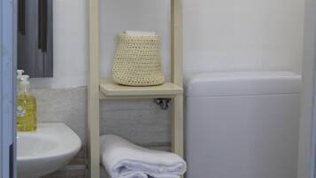 Une salle de bain avec un lavabo blanc, des toilettes et une étagère où sont posées des serviettes et une bouteille.