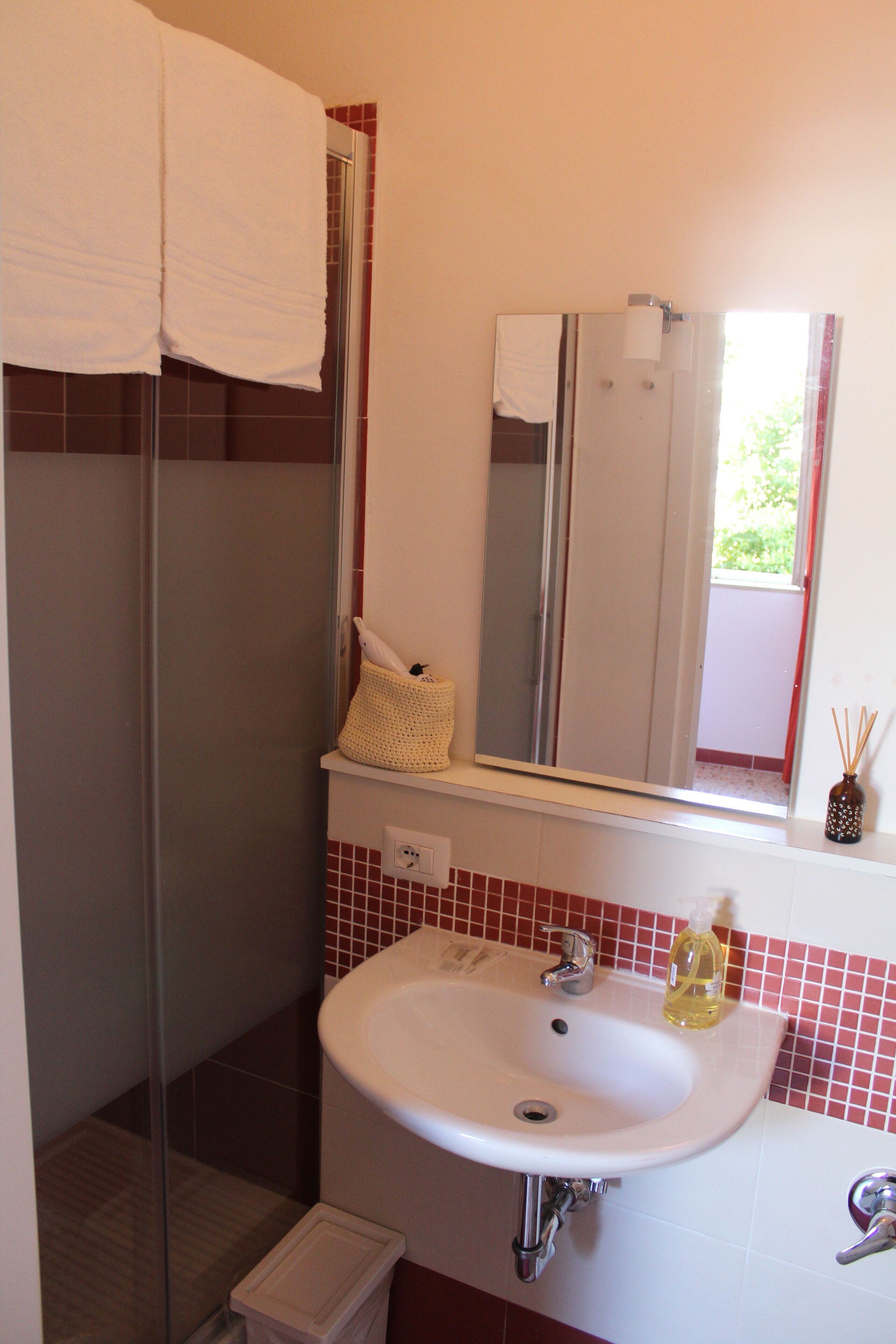 Une salle de bain avec un lavabo blanc, une cabine de douche en verre, un miroir et une serviette accrochée au mur.