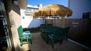 A patio with a table and chairs, a thatched umbrella, and a wooden fence.