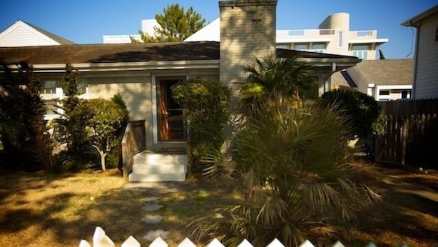 A residential house with a front porch, a white picket fence, and a palm tree in the yard.