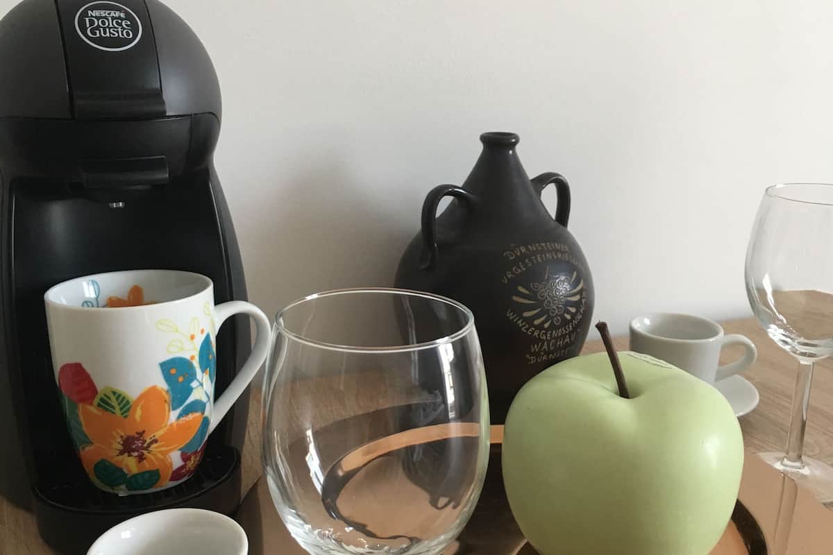 A coffee maker, a teapot, a cup, a wine glass, and an apple on a tray.