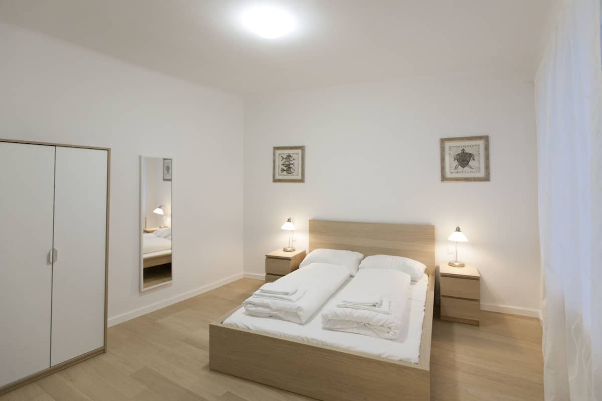 A bedroom with a wooden bed, two bedside tables with lamps, a wardrobe, and two framed pictures on the wall.
