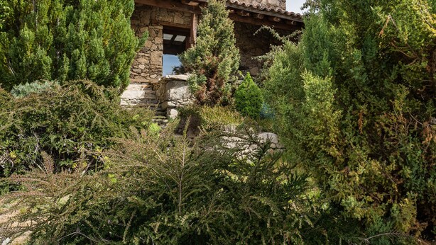 Un edificio de piedra con tejado de baldosas, rodeado de abundante vegetación.