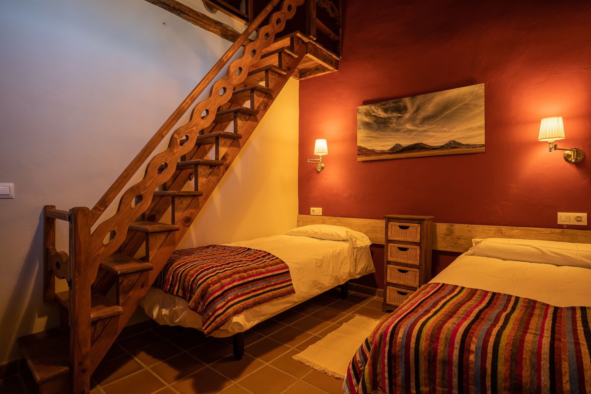 A bedroom with two beds, a wooden staircase, and a painting on the wall.