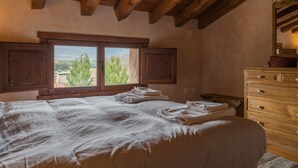 Un dormitorio con una cama grande, vigas de madera en el techo, una ventana con vistas y un aparador de madera.