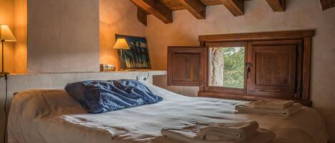 Un dormitorio con una cama grande, vigas de madera, un cuadro y una ventana con vista a árboles.