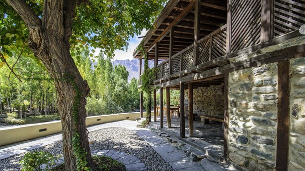 Un edificio de piedra con un balcón de madera, rodeado de árboles y un sendero de piedra.