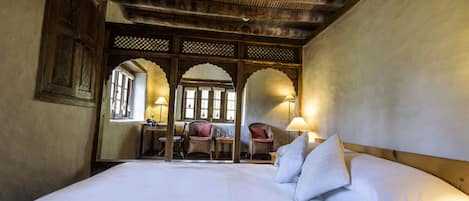 Une chambre de style traditionnel, dotée d’un grand lit, de meubles en bois et offrant une vue à travers une fenêtre en arc de cercle.