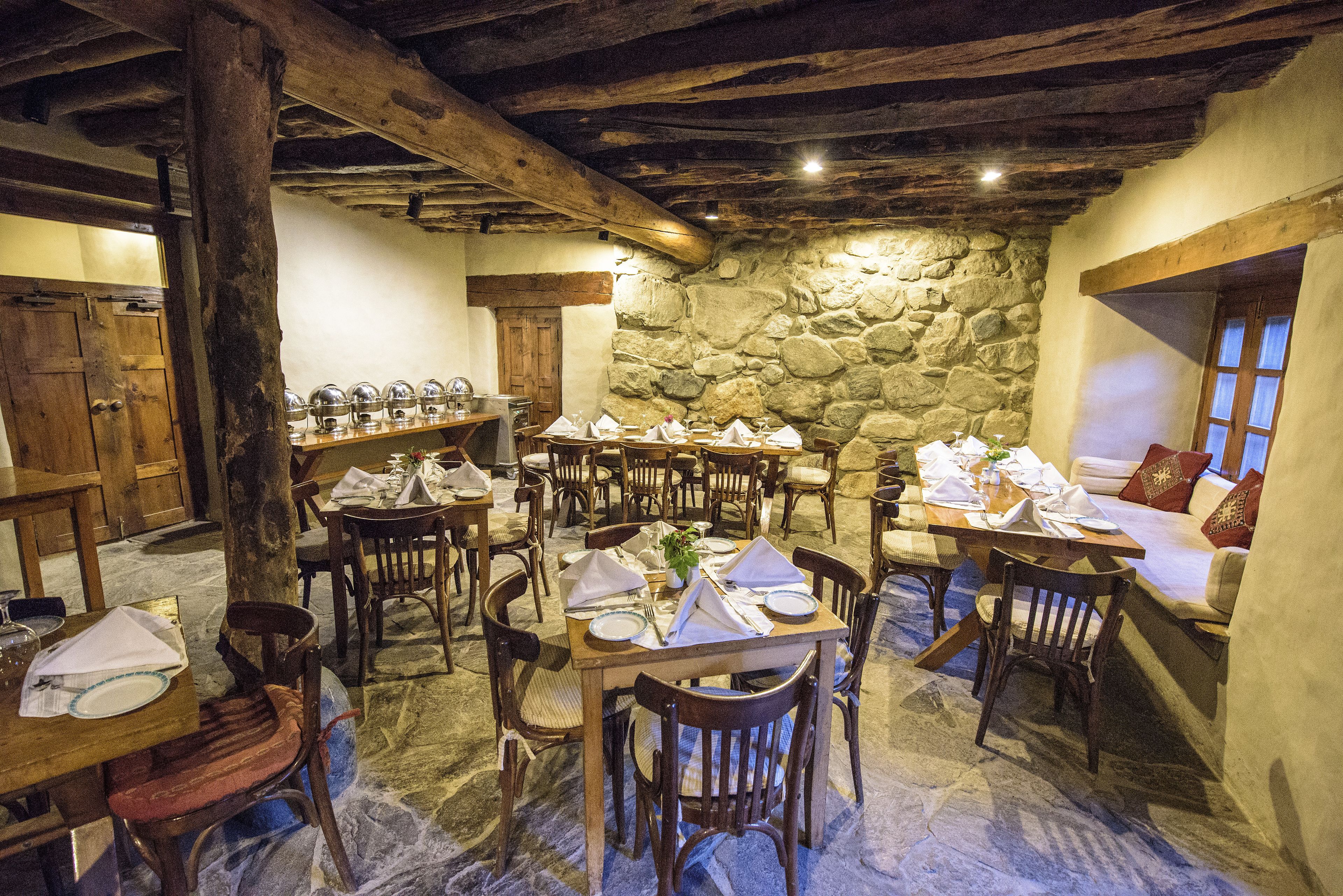 Un coin repas rustique avec des tables et des chaises en bois, des murs en pierre et des poutres apparentes.