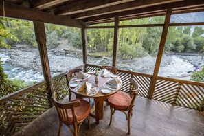 A wooden table set for four with chairs, overlooking a river and forested area. - Serena Shigar Fort (Shigar)