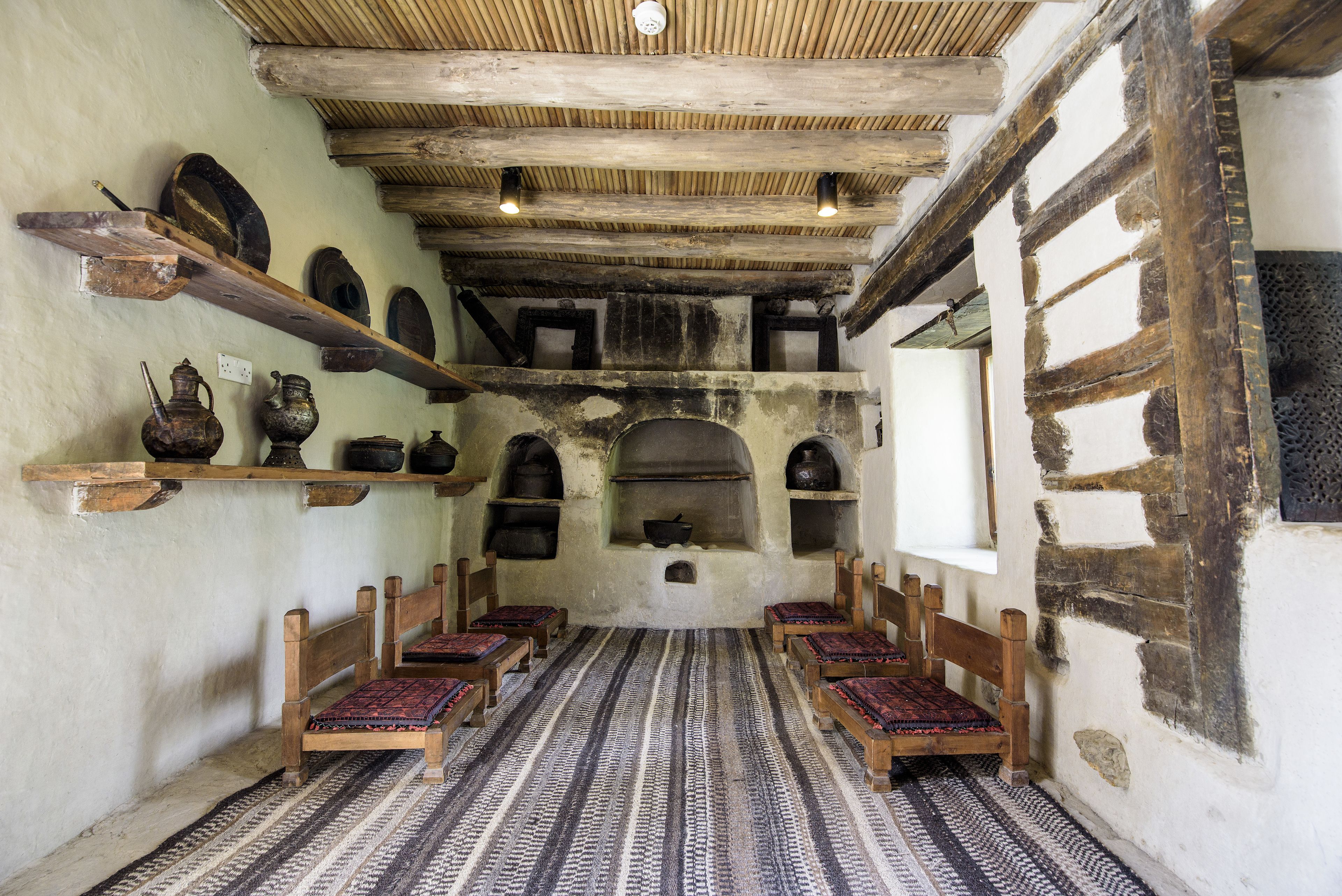 A room with wooden benches, a patterned carpet, and shelves with pottery.