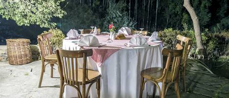 Un área de comedor al aire libre con una mesa dispuesta para cuatro personas, sillas de madera alrededor y una cesta a un lado.