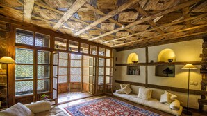 Una habitación tradicional con techo de madera, un ventanal con vidrio emplomado, un sofá y una alfombra estampada.