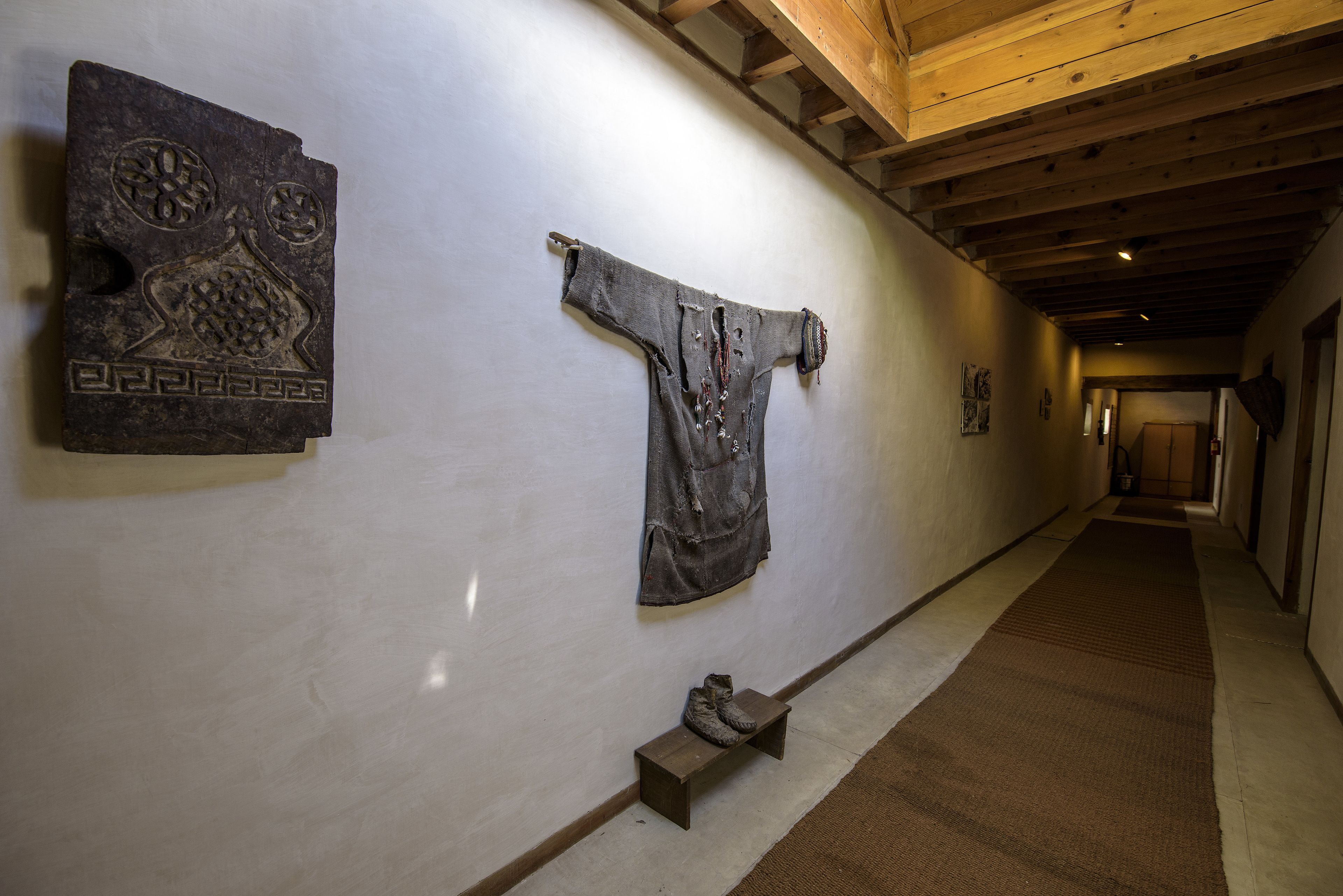 A hallway with a wooden ceiling, a bench with a pair of boots, and two artworks on the wall.